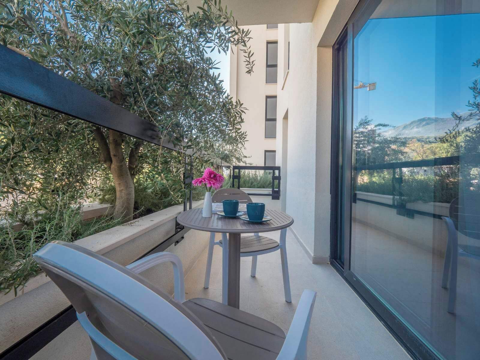 A balcony with a table and chairs, a potted plant, and a view of a building and landscape.