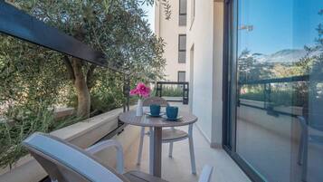 A balcony with a table and chairs, a potted plant, and a view of a building and landscape.