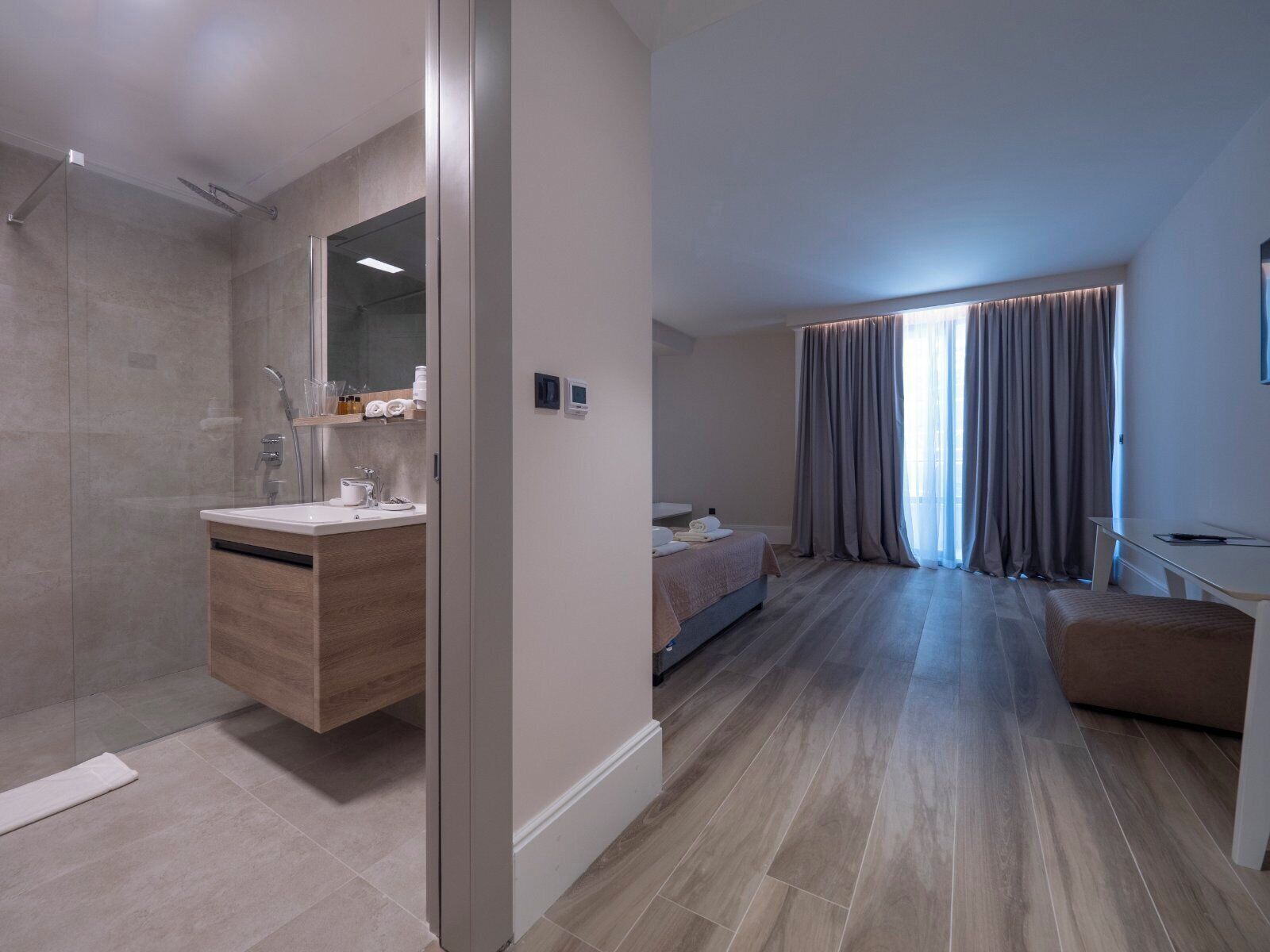 A modern hotel room with a shower, a vanity with a mirror, a bed, and a desk.