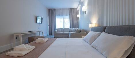 A hotel room with a large bed, a sofa, a desk, and a TV.