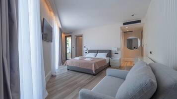 A modern hotel room with a large bed, a sofa, a desk, and a bathroom visible through an open door.