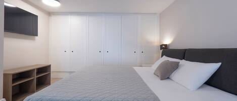 Quarto moderno com cama, televisão fixada na parede e guarda-roupa com várias portas.