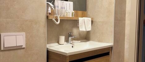 A modern bathroom with a wooden vanity, a white sink, and a mirror above it. There is a towel hanging on the wall and a toilet with a white lid.