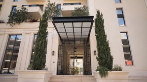 A building entrance with a covered walkway, steps leading up to it, and two symmetrical trees in planters. - CASA AL MARE by Moskva (Becici)