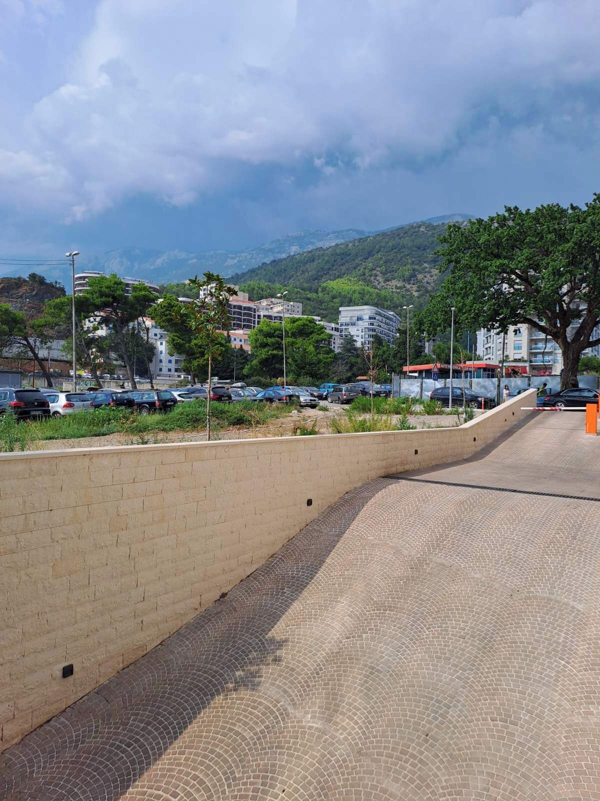 A paved walkway with a brick wall on one side and a parking lot with cars in the background.