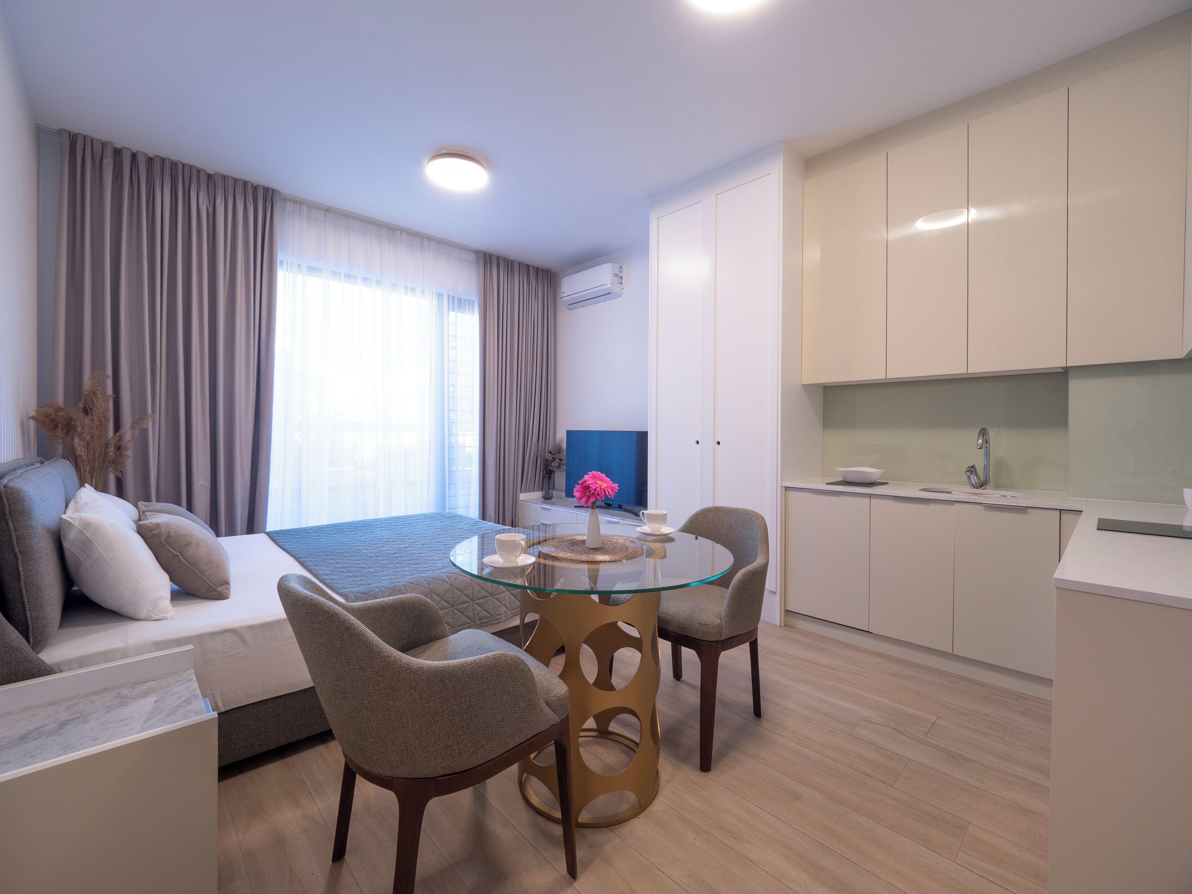 Une chambre d’hôtel moderne comprenant un lit, une table à manger en verre, deux chaises, un canapé, un téléviseur et un coin cuisine.