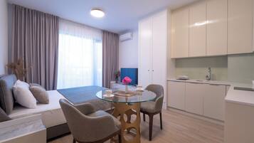Une chambre d’hôtel moderne comprenant un lit, une table à manger en verre, deux chaises, un canapé, un téléviseur et un coin cuisine.