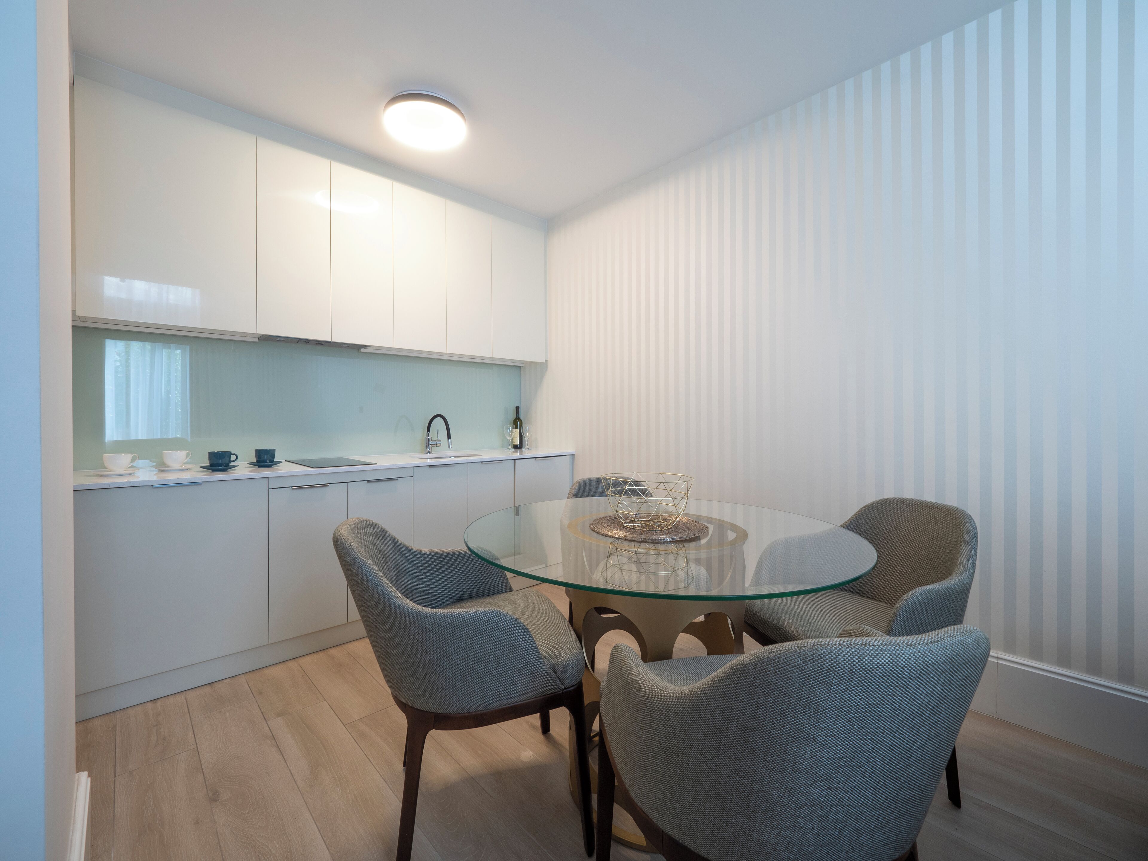 Una cocina moderna con armarios blancos, una mesa de comedor de vidrio y dos sillas tapizadas en gris.