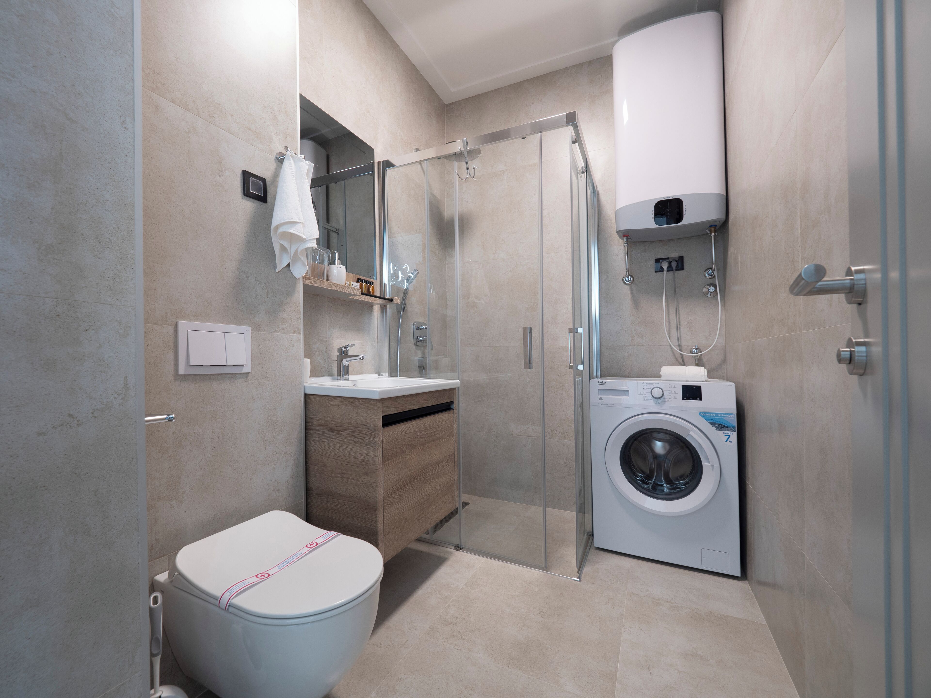 Een moderne badkamer met toilet, wastafel, spiegel, douche en een ingebouwde wasmachine.