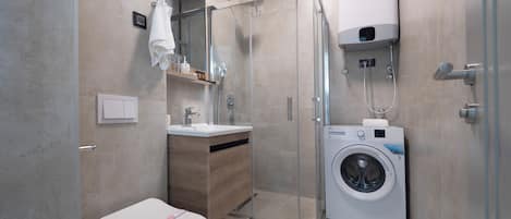 Een moderne badkamer met toilet, wastafel, spiegel, douche en een ingebouwde wasmachine.