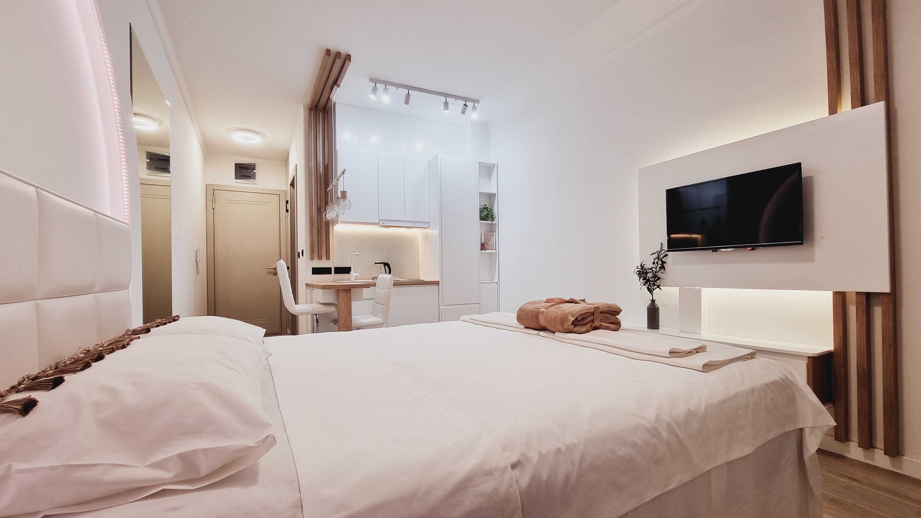 Una habitación de hotel moderna con una cama grande, un escritorio con silla, un televisor montado en la pared y un baño visible a través de una puerta abierta.