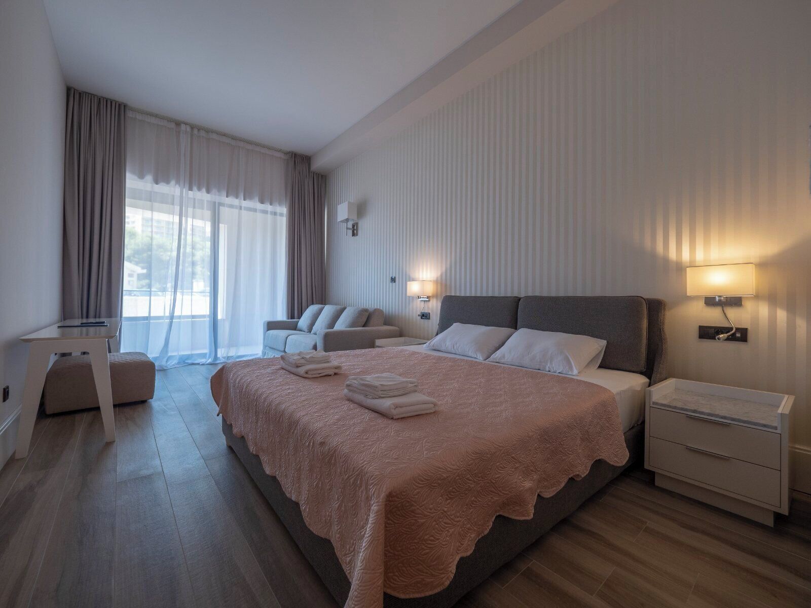 A modern hotel room with a large bed, a seating area, and a view of the outdoors.