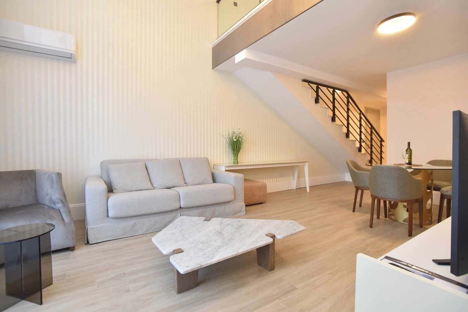 A modern living room with a grey sofa, a marble coffee table, and a dining area with chairs and a table.