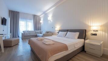Quarto de hotel moderno com uma cama grande, um sofá, uma escrivaninha e uma televisão.