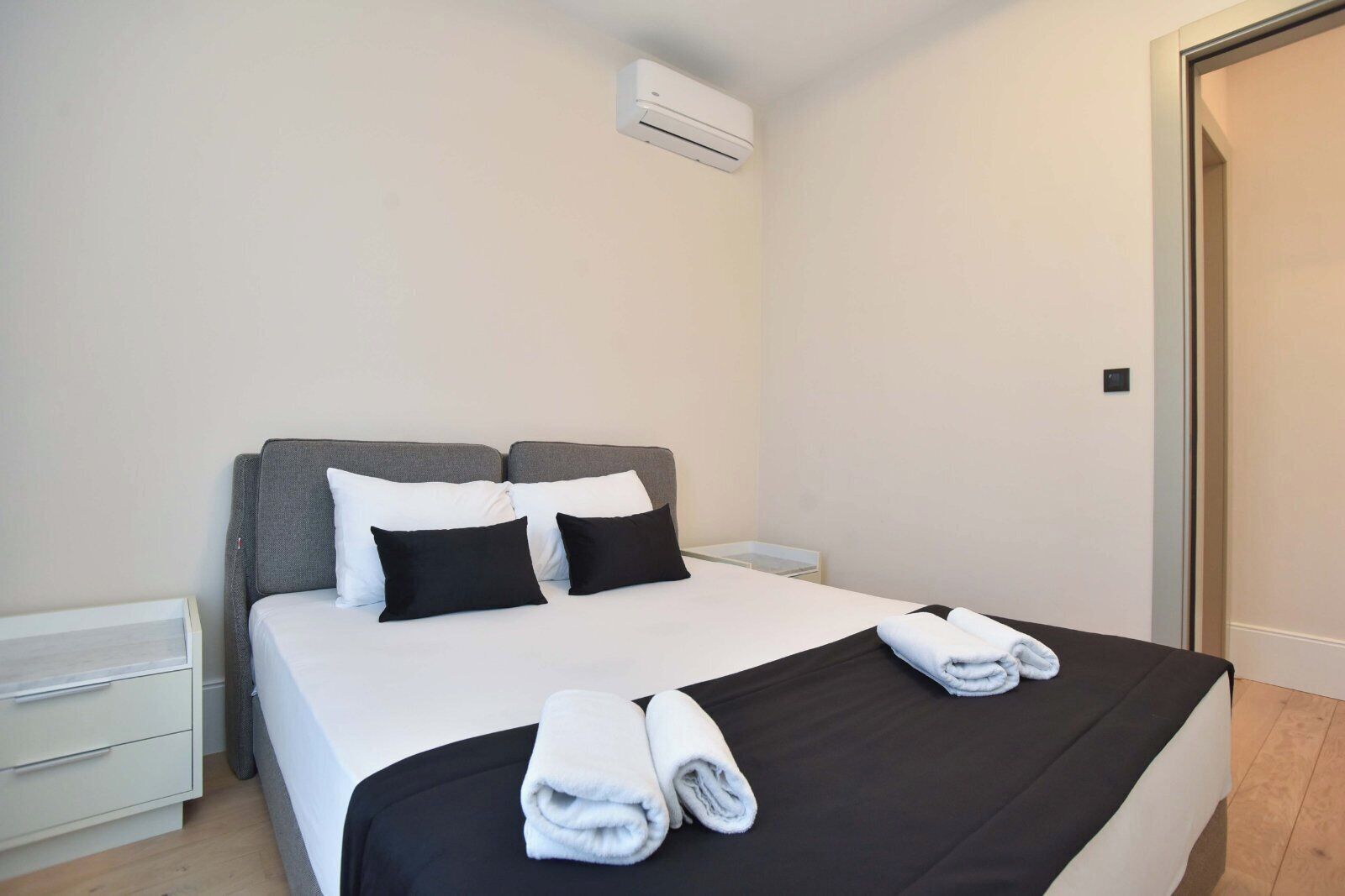A hotel room with a bed, two pillows, a nightstand, a drawer, and a towel on the bed.