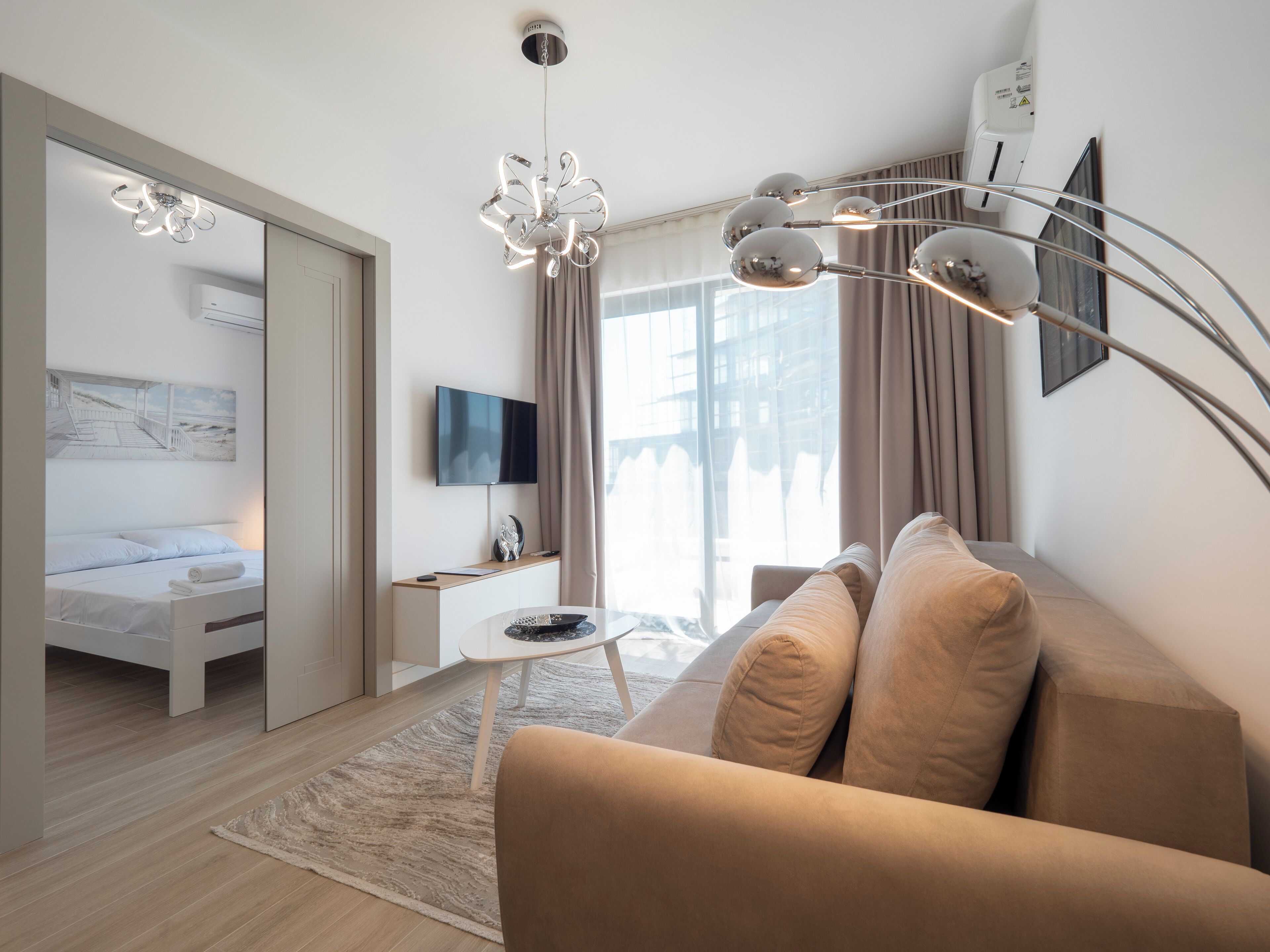 Una habitación de hotel moderna con sofá, televisor, escritorio y ventana grande.