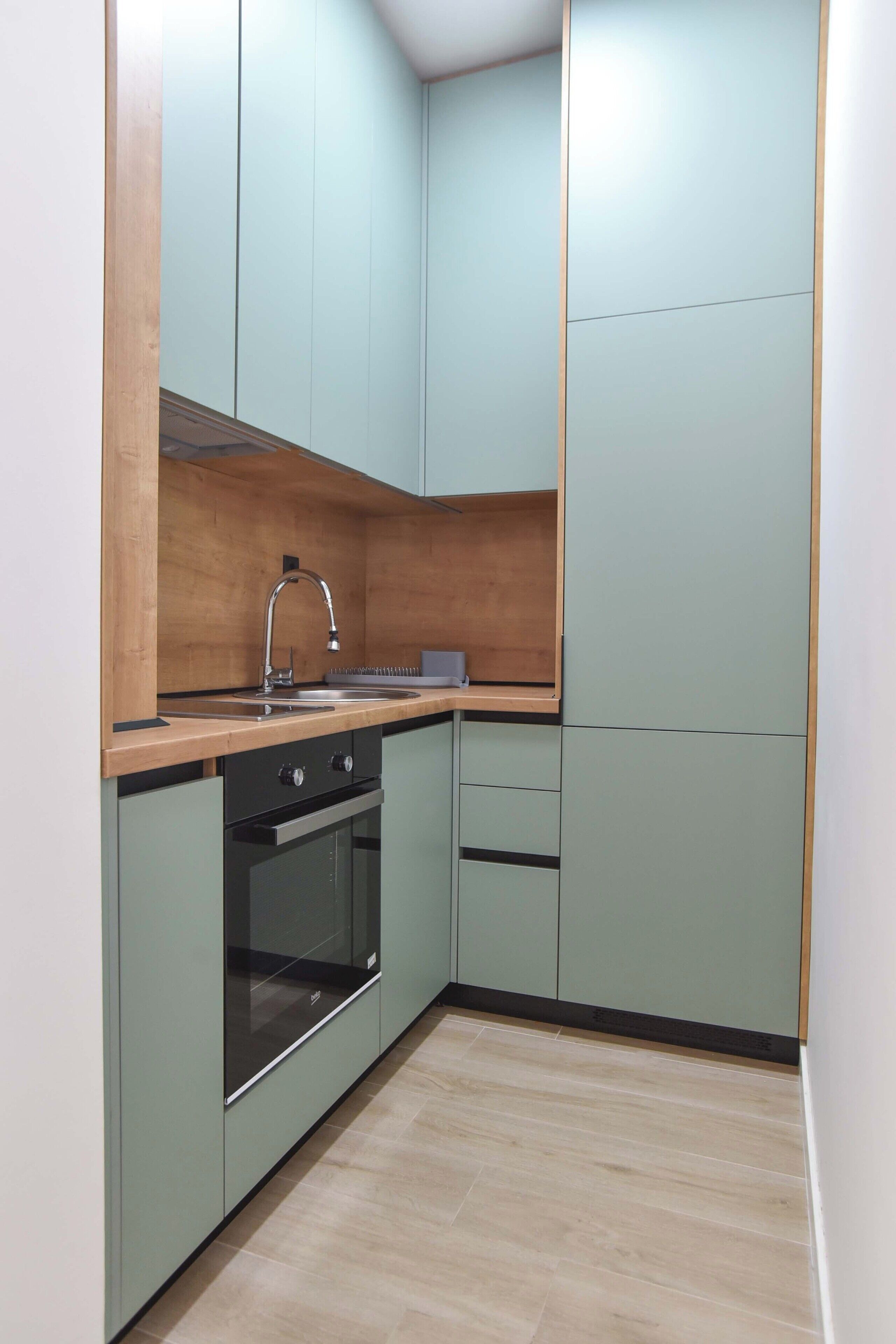 Una cocina compacta con encimera de madera, un fregadero, un horno y armarios verdes.
