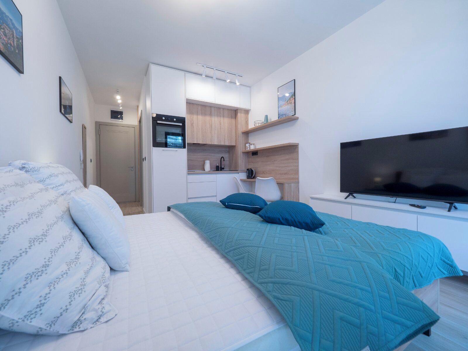 Une chambre moderne équipée d’un lit, d’une télévision, d’un coin cuisine et d’une porte donnant sur une autre pièce.