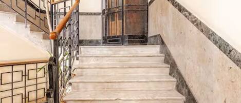 A staircase with a metal railing and a wooden handrail, leading to a door with a metal grille.