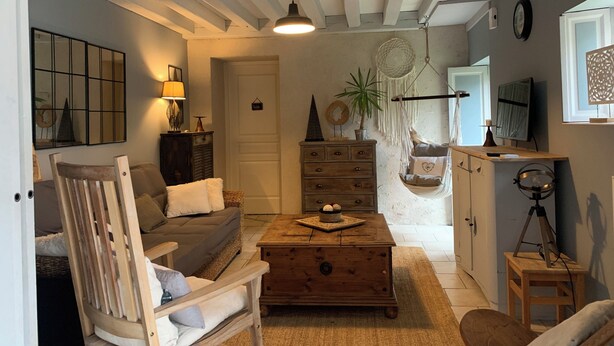 A cozy living room with a wooden sofa, a wooden coffee table, a hanging macrame chair, a dresser, and a television on a stand. - Charming house close to the Loire châteaux (Baule)
