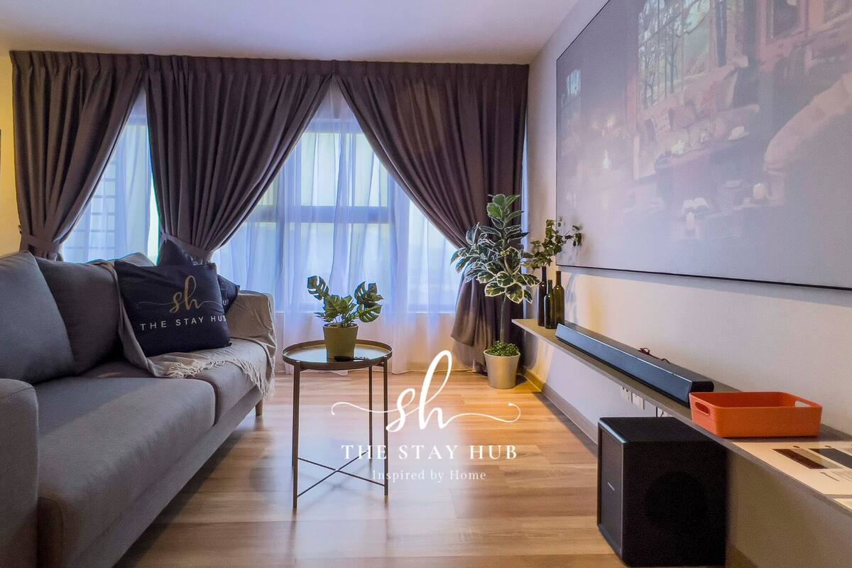 Een moderne woonkamer met een grijze bank, een salontafel, een plant in pot en een aan de muur bevestigde televisie.