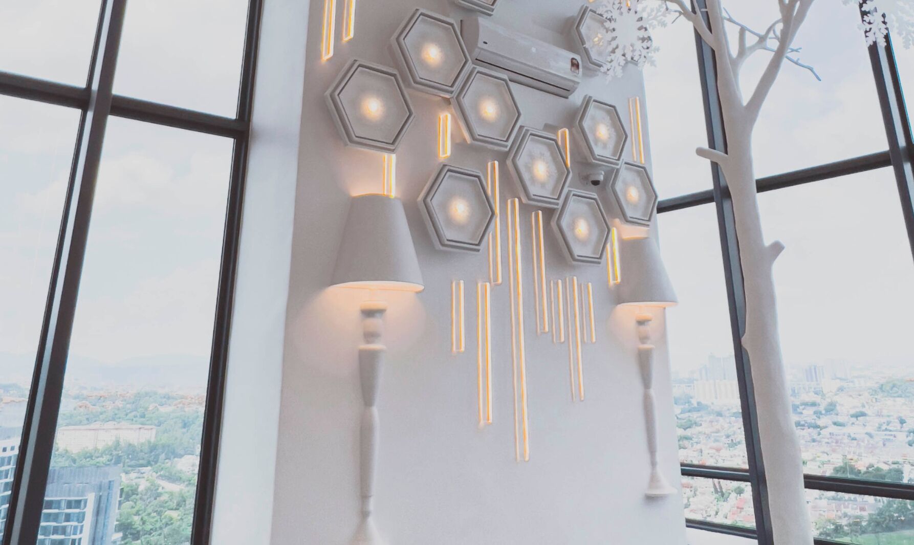 A modern interior with hexagonal light fixtures and a view of a cityscape through large windows.