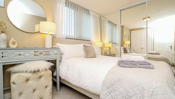 A hotel room with a large bed, a bedside table, a mirror, and a window with curtains. - Modern Apex Flat / King Bed/3 Guests/ Parking/WiFi (Argyll and Bute Council)