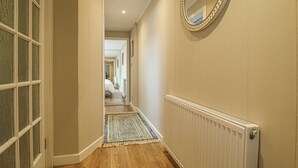 A hallway with a wooden floor, a radiator, and a mirror on the wall. - Modern Apex Flat / King Bed/3 Guests/ Parking/WiFi (Argyll and Bute Council)
