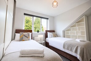 A hotel room with two beds, a window with a view of trees, a bedside lamp, and a geometric light fixture.