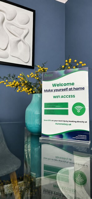 A welcome sign with WiFi access instructions, a vase with yellow flowers, and a framed artwork on a wall.