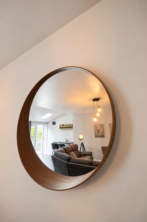 A round mirror with a wooden frame reflecting a living room interior.