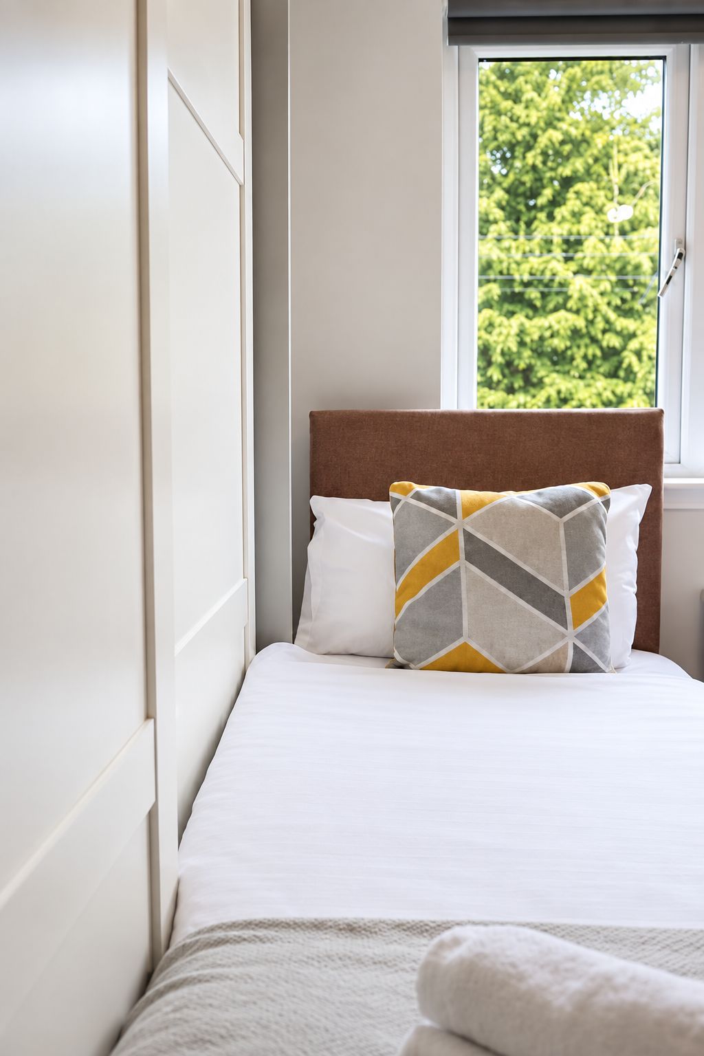 Comfortable single bed with fresh linen, soft pillows and a bright window overlooking leafy surroundings.