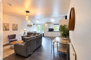 A modern living room with a sofa, a dining table, and a kitchen in the background.