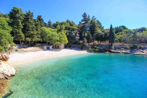 A beach with clear turquoise water, trees, and a stone structure.