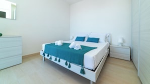 Een moderne slaapkamer met een bed, nachtkastje, dressoir en spiegel.