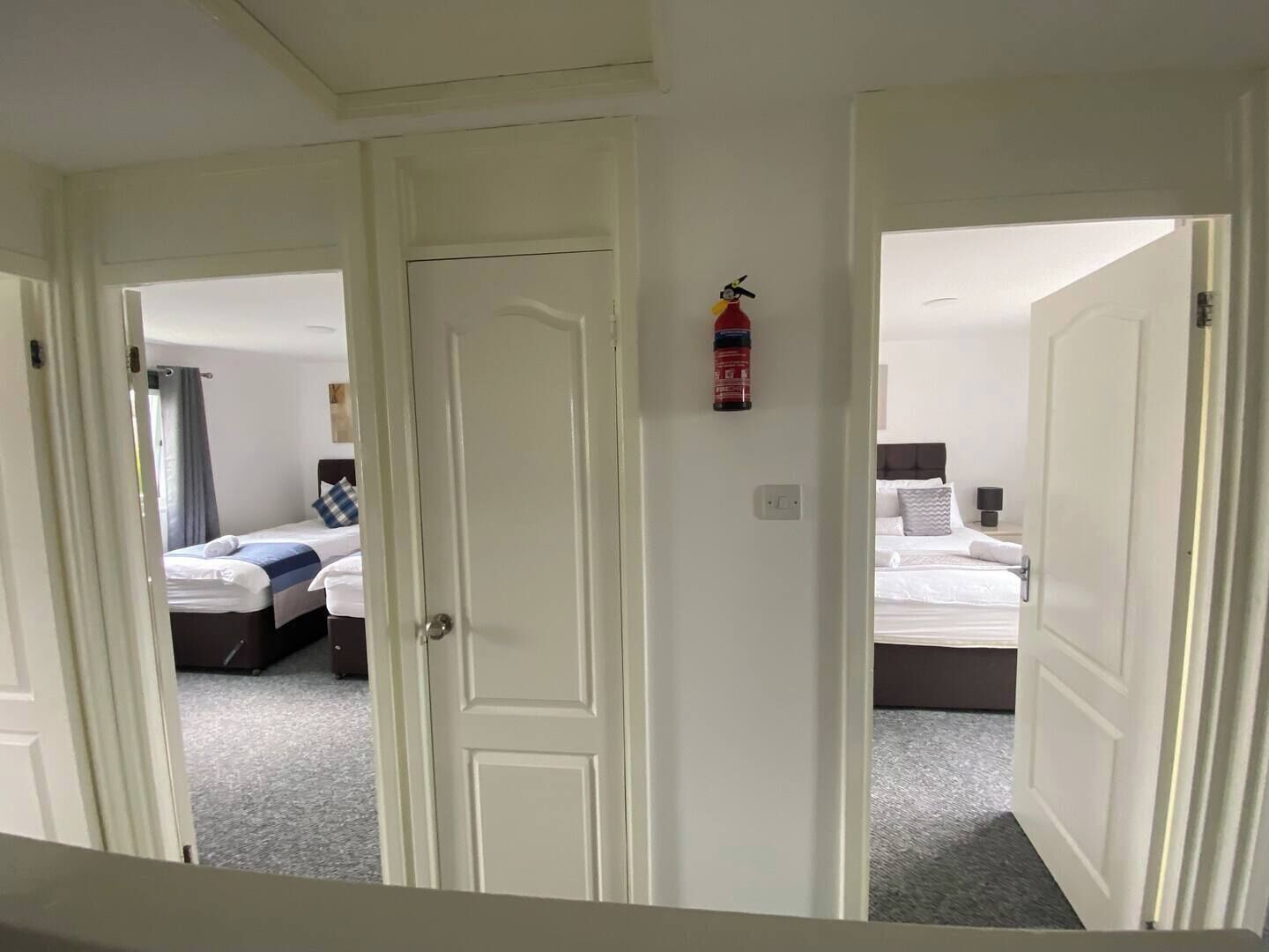 A hotel room with a bed, a nightstand, and a wall-mounted fire extinguisher.