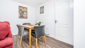 A dining area with a wooden table, two grey chairs, a red sofa, and a white door.