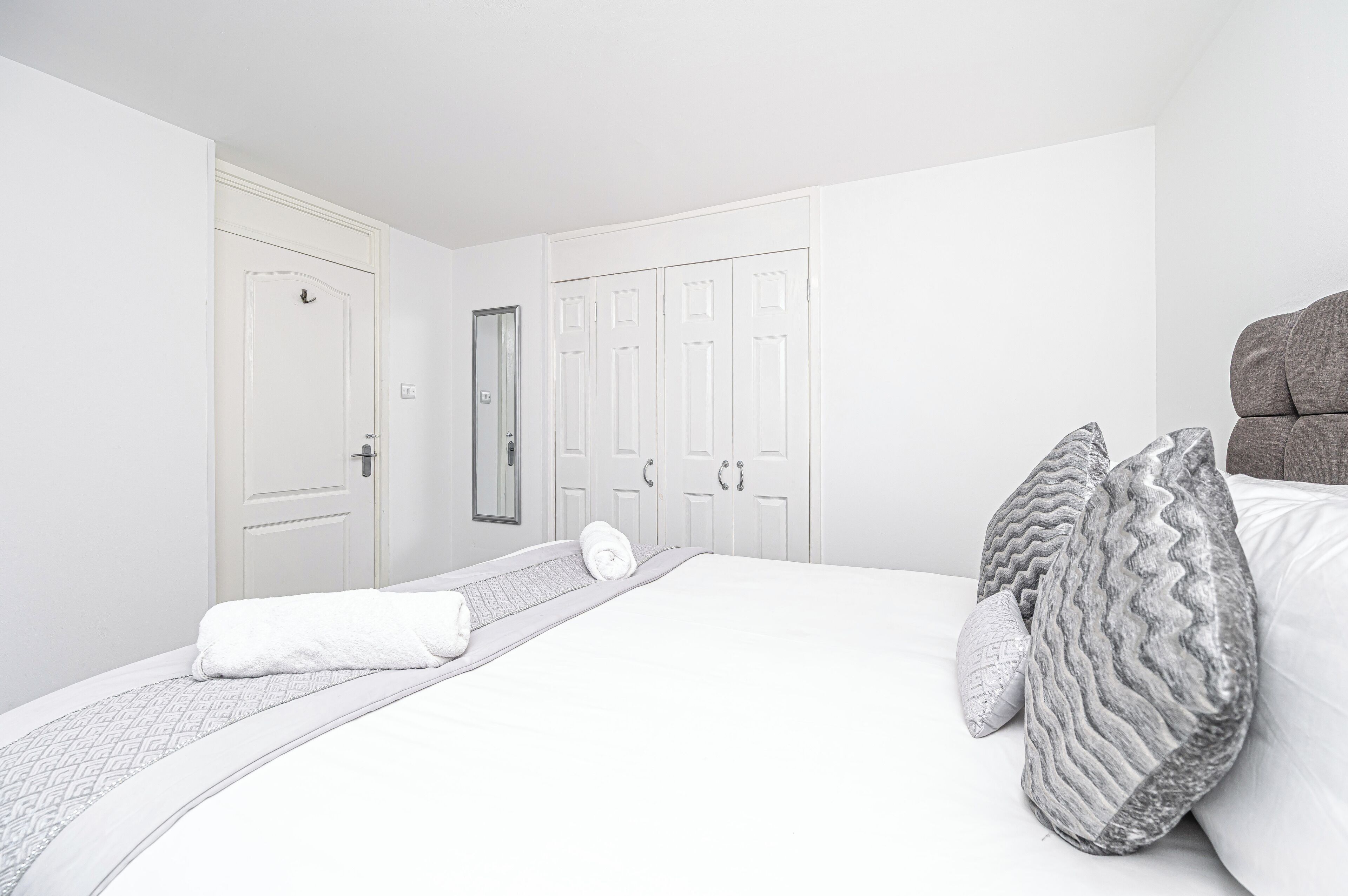 Una camera d'albergo con un letto rifatto, un comodino e un armadio con uno specchio.