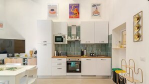 Et moderne køkken med hvide skabe, en mikroovn og en indbygget ovn. Der er et spiseområde med et hvidt bord og stole.