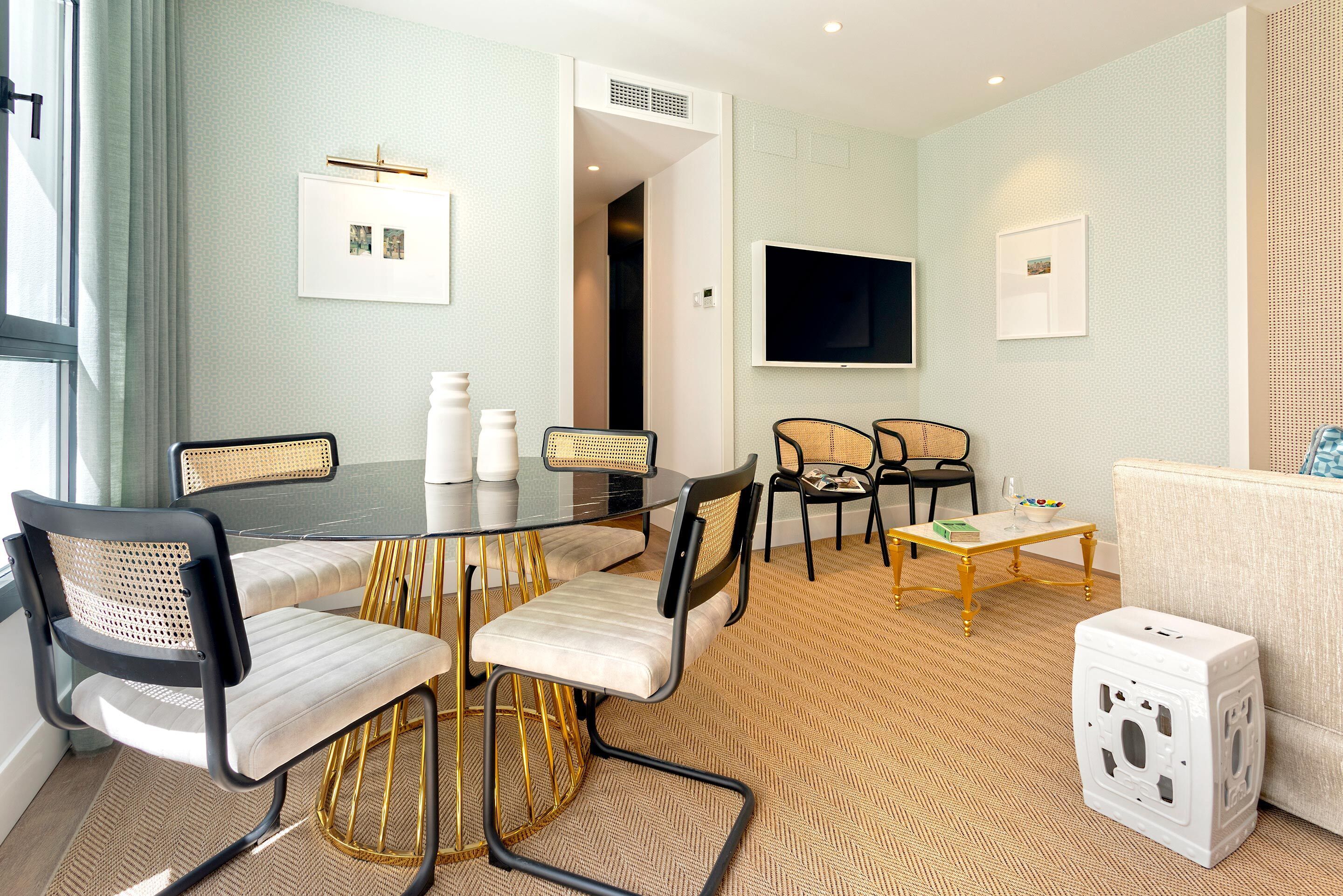 Una sala de estar moderna con una mesa de comedor, sillas, un sofá, un televisor y una mesita con objetos decorativos.