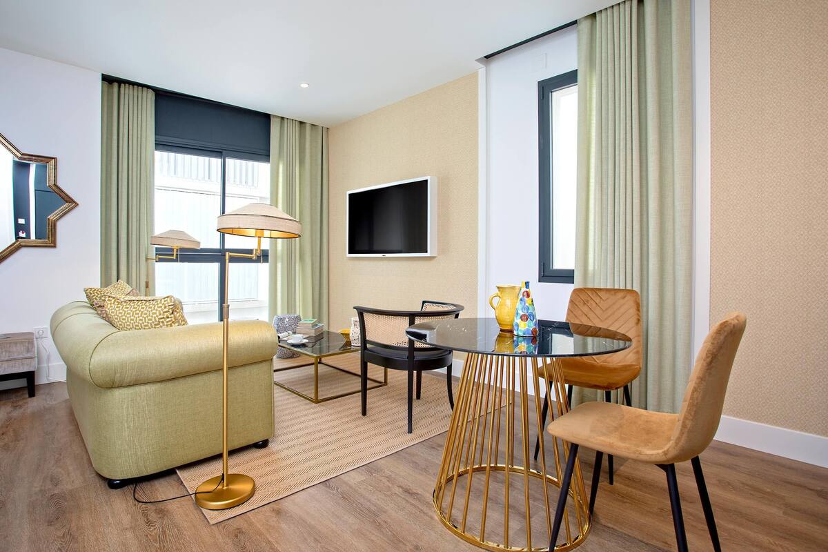 A modern living room with a sofa, a coffee table, a TV mounted on the wall, and a dining table with chairs.