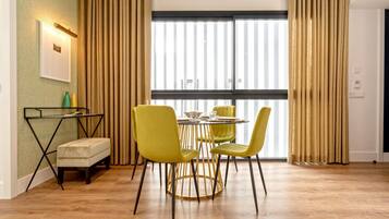 Un coin repas comprenant une table ronde, quatre chaises jaunes, un petit banc, une table avec un plateau en verre et un luminaire fixé au mur.