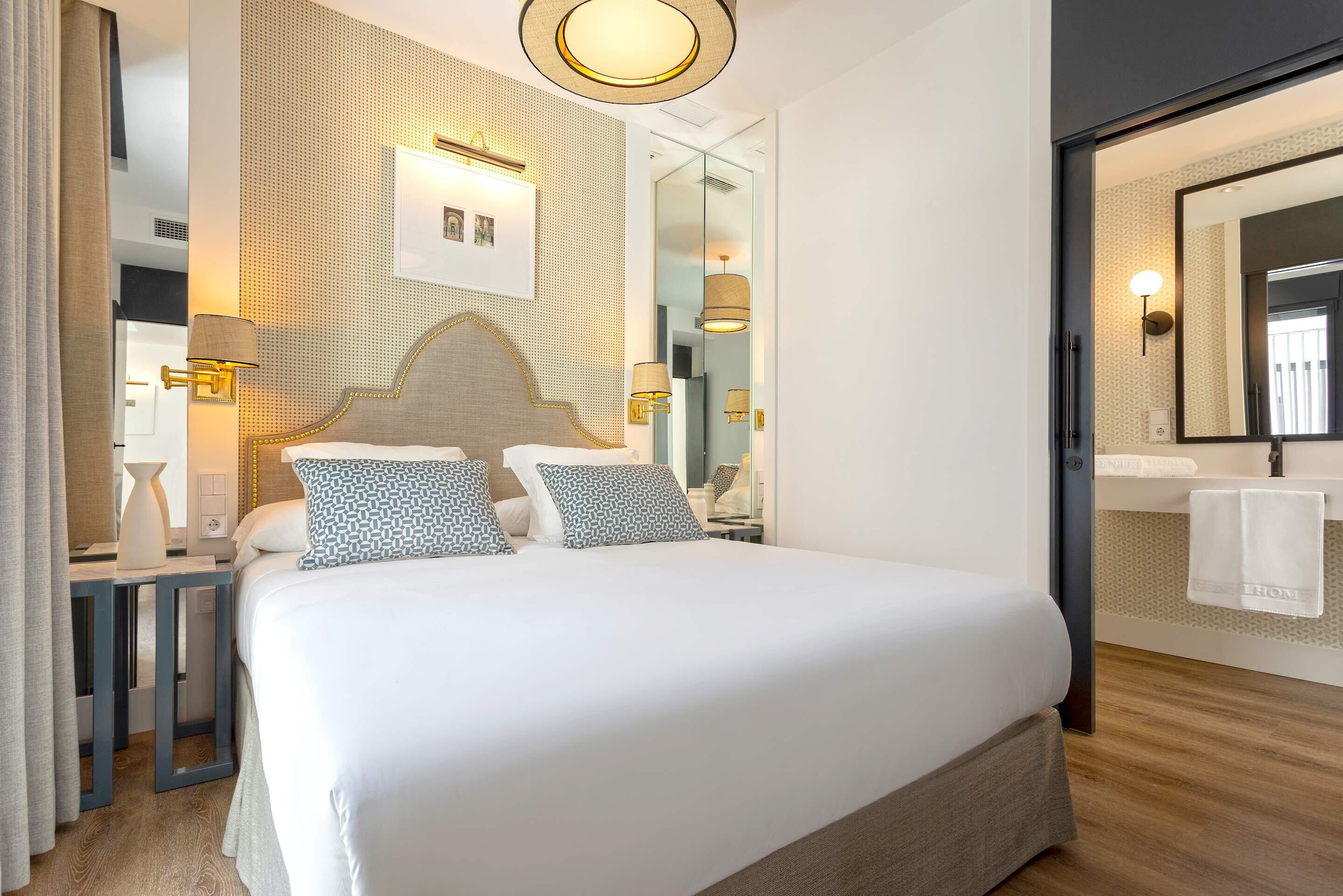 Una habitación de hotel moderna con una cama grande, un espejo y una mesita de noche con una lámpara.