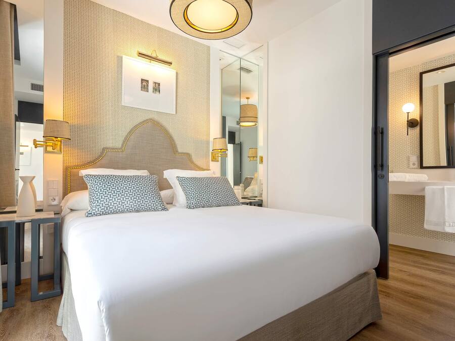 Una habitación de hotel moderna con una cama grande, un espejo y una mesita de noche con una lámpara.