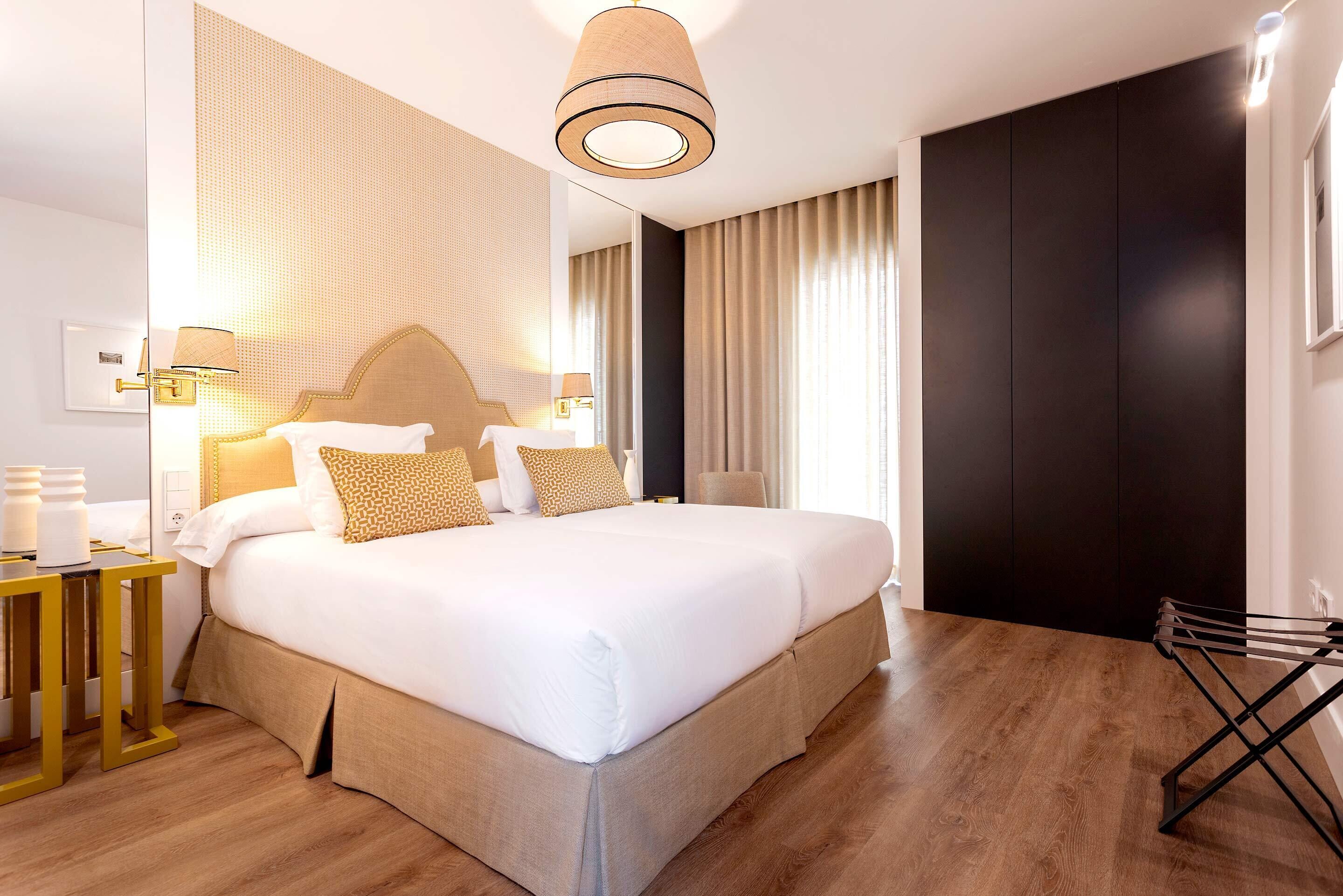 Una habitación de hotel moderna con una cama grande, una mesita de noche con lámpara, un armario y una percha.