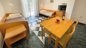Habitación compacta con cama, sofá, mesa de comedor con sillas, televisor y balcón con cortinas.