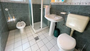 Un baño con inodoro, bidé, ducha, lavamanos y espejo.