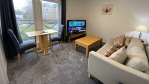 Un salon avec un canapé, une petite table, un téléviseur et une fenêtre avec des rideaux.