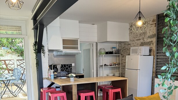 A modern kitchen with white cabinets, a wooden countertop, and red bar stools. There is a blue sofa with cushions and a yellow pillow in the living area. - Apart 50m² 5 People 2 Bedrooms –Town, Train, Beach few mn (La Bernerie-en-Retz)