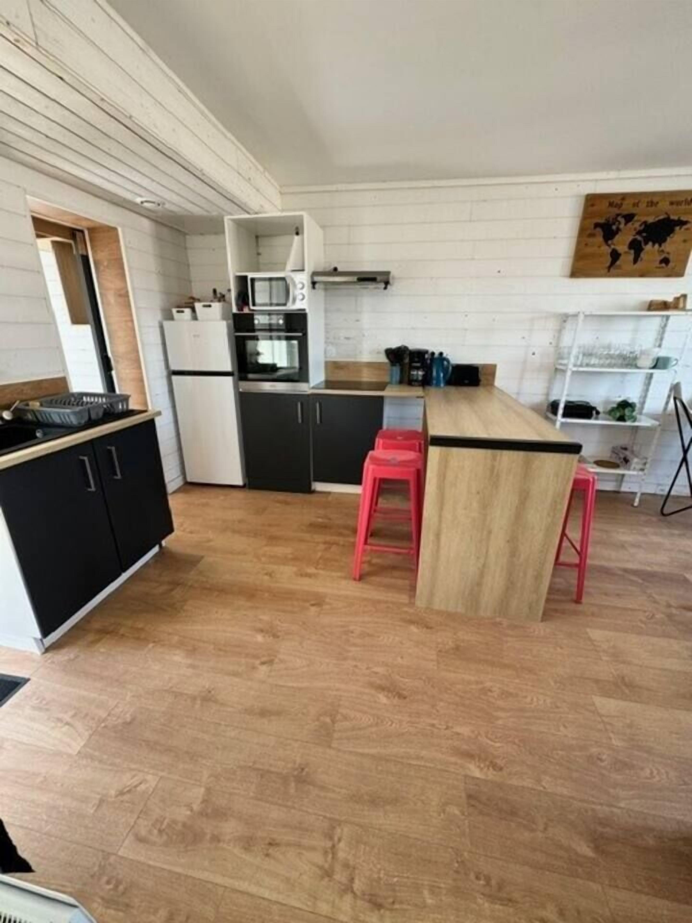 Une cuisine compacte dotée d’un îlot central, de meubles noirs et d’un tabouret rouge.